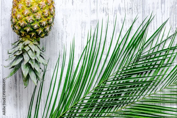 Fototapeta Pineapple and palm branch on wooden desk background top view