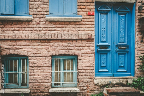 Fototapeta ISTANBUL,TURKEY - May 6,2017:Facade view of vintage style old red brick wall house with blue door and turquoise window. Vintage building and old aged design in Balat,Istanbul,Turkey.