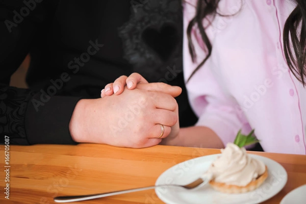 Fototapeta Young beautiful couple is holding each other's hands in a cafe