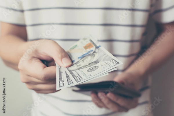 Fototapeta Hand of man holding a spread of cash us dollar bill with money pouch, Vintage tone picture