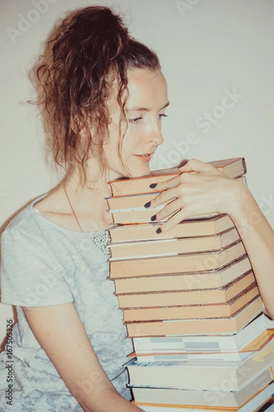 Fototapeta Satisfied student girl holding high stack of books. Education and learning concept. Invest time in studies. Time to upgrade ideas. Increase knowledge. Back to school, university. Exams preparation.