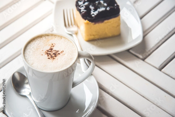 Fototapeta A cup of latte, cappuccino or espresso coffee on a white wood table and a Blueberry Cheesecake.