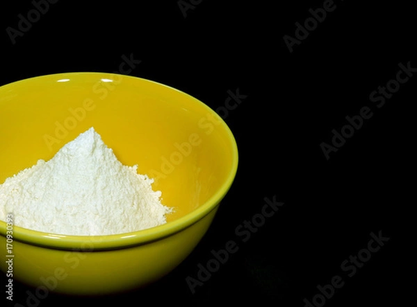 Fototapeta Pure white raw flour in yellow ceramic mixing bowl, isolated on black background with free space for design and text 