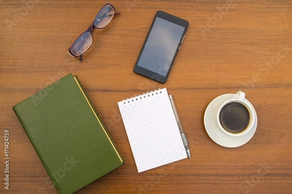 Fototapeta Cup of coffee, book, notepad, pen, eyeglasses and smart phone on wooden desk