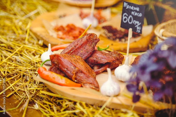 Fototapeta jerky with garlic and pepper composition on straw and wood, rustic style, selling meat