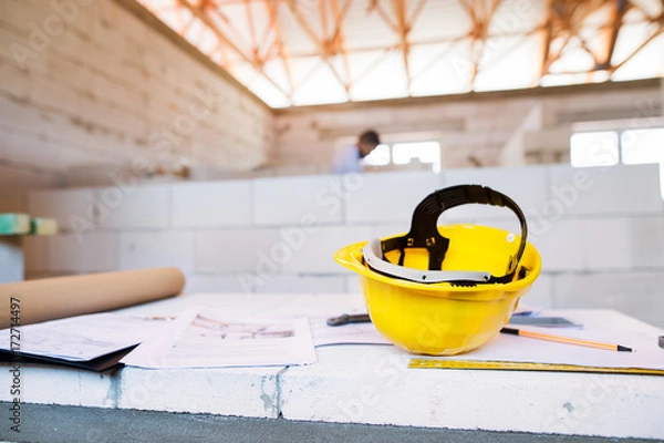 Fototapeta Helmet and blueprints on construction site.