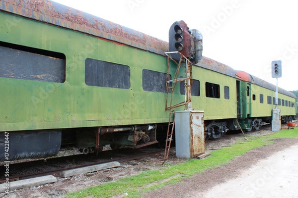 Fototapeta Green abandoned passenger train cars with boarded windows beside light posts on train tracks
