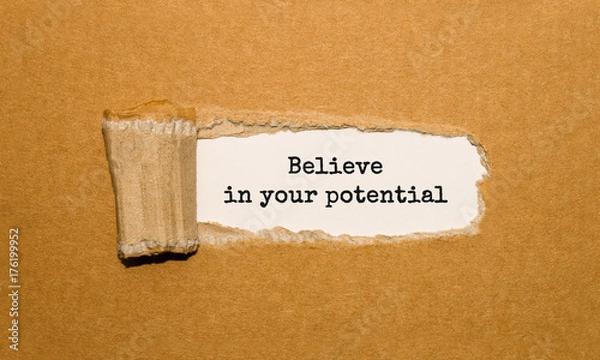 Fototapeta The text Believe in your potential appearing behind torn brown paper