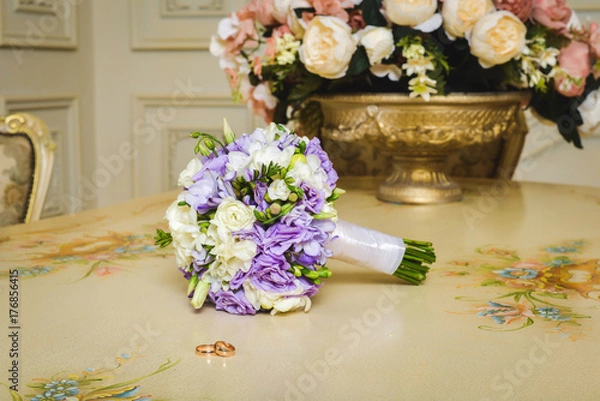 Fototapeta Wedding bouquet of the bride on a wooden table where engagement rings lie. Bridal bouquet on the background of an old vase with flowers in the apartments.