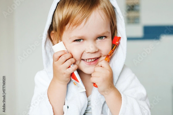 Fototapeta Portrait of a cute child with toothbrush and toothpaste in the bathroom.