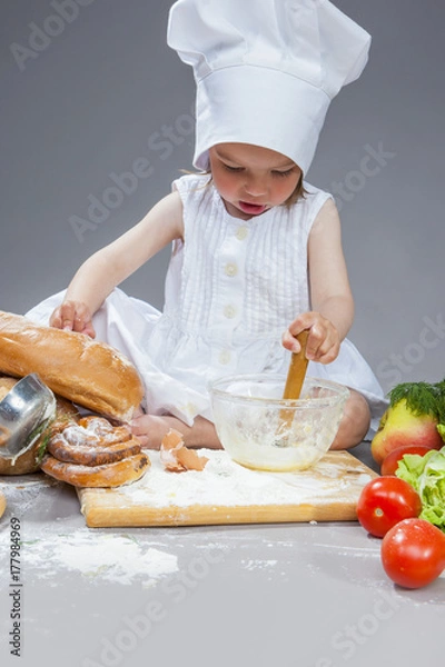 Obraz Cooking Ideas. Caucasian Little Girl In Cook Uniform Working With Whisk and Kitchen Glassware In Studio Environment. With Vegetables and Fruits on Background.