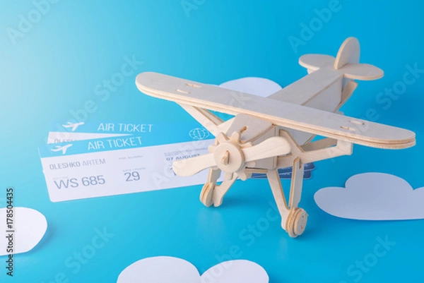 Fototapeta Wooden toy airplane and tickets on a background of blue sky with paper clouds. Concept travel and airlines