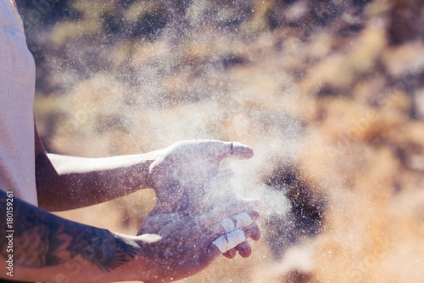 Fototapeta Dark skinned woman with arm tattoos and taped tingers claps her hands with chalk before a rock climb