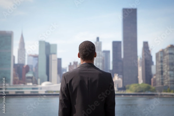 Fototapeta Back view of ambitious young African American business man looking at NYC skyline, contemplating