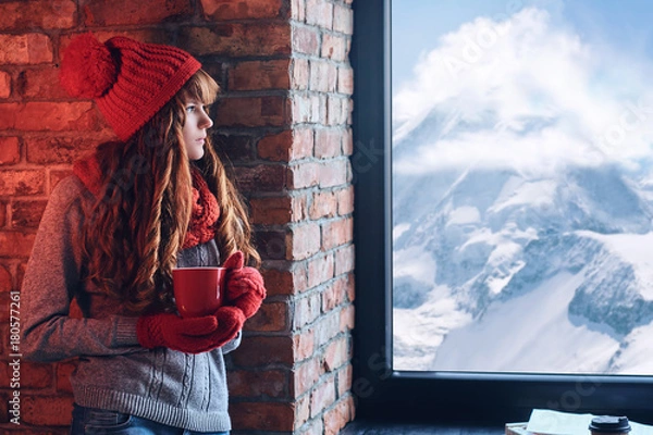 Fototapeta A woman holds coffee and looking over the window on a winter mou