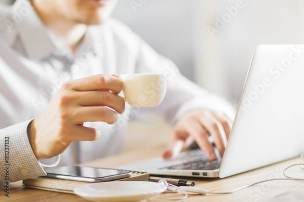 Fototapeta Man drinking coffee using laptop