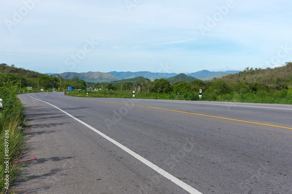 Fototapeta Stretched road along with trees and scenic view of mountain and blue sky