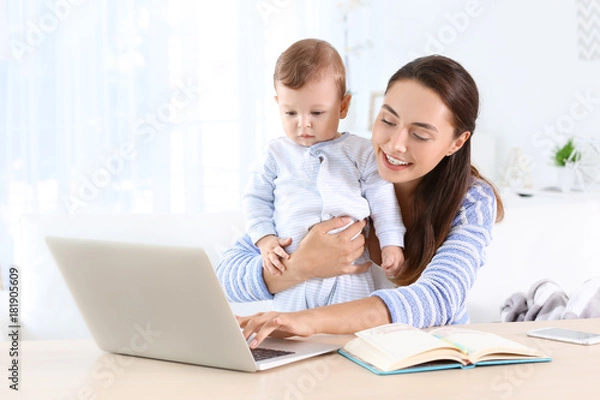 Fototapeta Young mother holding baby while working in home office