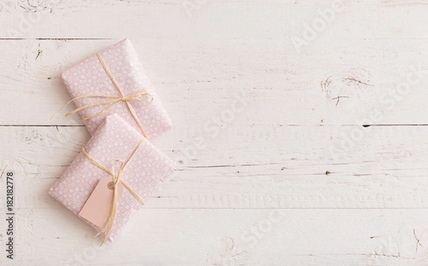 Fototapeta Top view on small gifts wrapped in pink paper with ribbons and tag on white wooden background. Present for birthday, Christmas or any other celebration or party