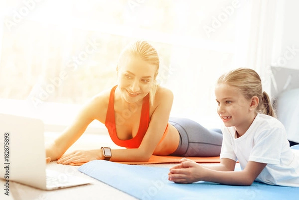 Fototapeta Mother and daughter are engaged in yoga in sportswear. They are in a bright room with panoramic windows.