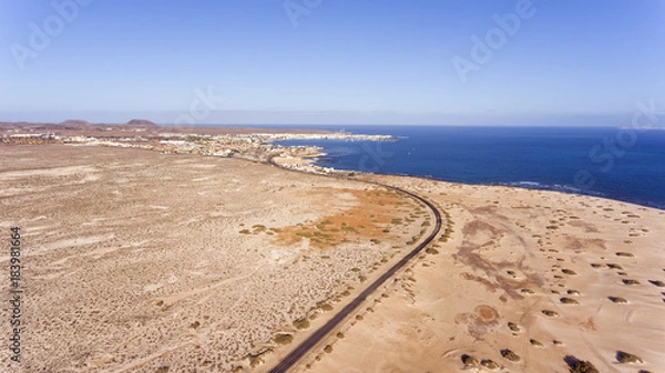 Fototapeta Aerial view of road going through white sand beach, dunes towards tourist resort of Corralejo, , Fuerteventura, Canary Islands, Spain .