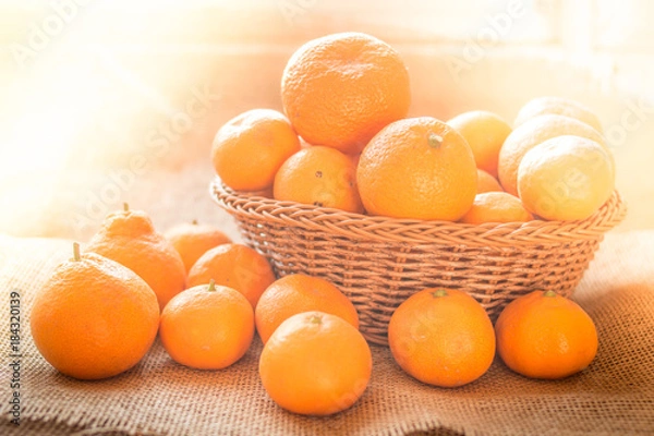 Fototapeta Fresh ripe fruit tangerine oranges in a basket with rustic background and with morning sunlight effect.