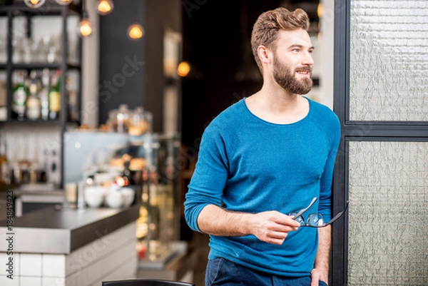 Fototapeta Portrait of handsome man in blue sweater standing at the modern cafe interior