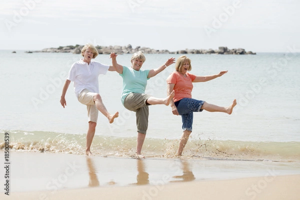 Fototapeta group of three senior mature retired women on their 60s having fun enjoying together happy walking on the beach smiling playful