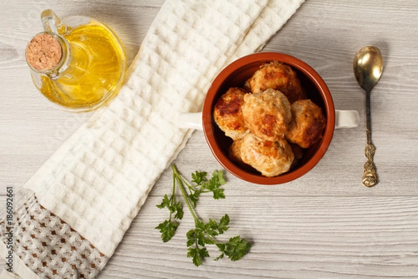 Fototapeta Fried meat cutlets in ceramic soup bowl, metal spoon, branch of fresh parsley, kitchen towel and glass bottle with sunflower oil. Top view