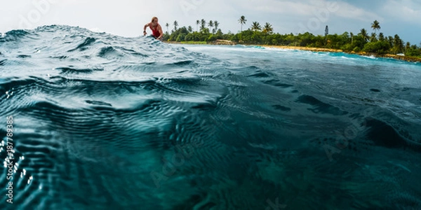 Fototapeta Surfer rides the ocean wave with palm trees on the background