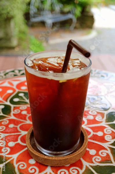 Fototapeta Glass of Iced Coffee on the Colorful Table at Garden Terrace with Selective Focus 