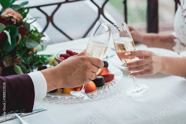 Fototapeta Glasses with champagne drink in bride and groom hands. Happy newlyweds drinking. Loving couple created new family.