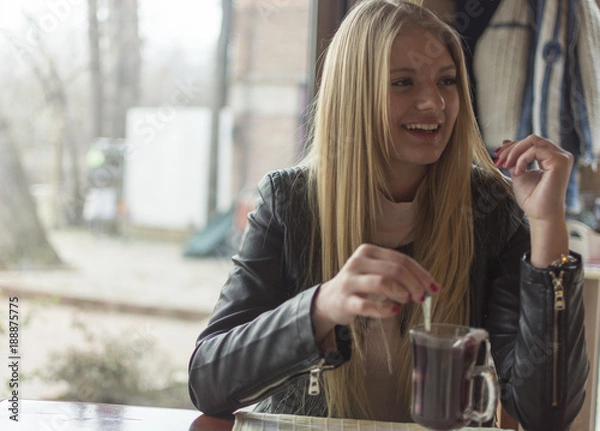 Fototapeta A beautiful young girl drinks tea in a restaurant and enjoys it