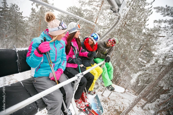 Fototapeta group of friends skier sitting at ski chair lift in beautiful sunny day. Concept of skiing