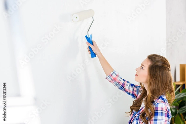 Fototapeta side view of girl painting wall with white paint