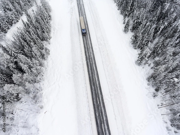 Fototapeta White semitrailer truck fast driving toward on slippery winter asphalt highway, aerial view from drone