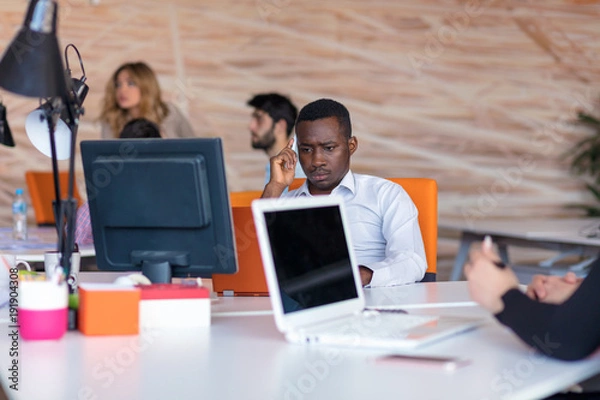 Fototapeta Frustrated young african entrepreneur with sad grimace in front of his laptop in office