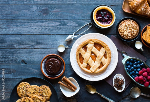 Fototapeta Top view of a wood table full of cakes, fruits, coffee, biscuits, spices and more