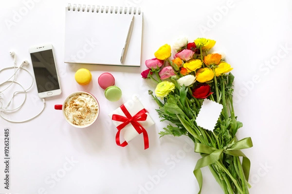 Fototapeta Festive morning concept buttercup flowers bouquet, gift box, cup of cappuccino, makarons cake, mobile, clean notebook, pen on the white background.