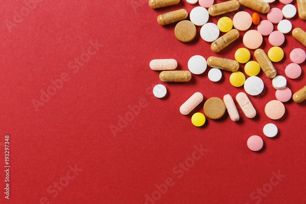 Fototapeta Medication white colorful round tablets arranged abstract on red color background. Aspirin, capsule pills for design. Health, treatment, choice healthy lifestyle concept. Copy space advertisement.