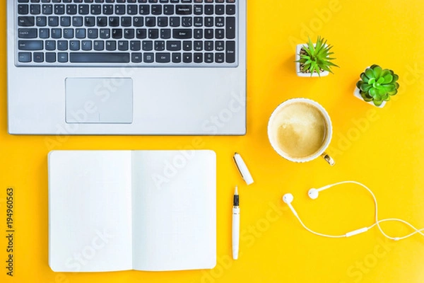 Fototapeta Workplace with a biclone, pen, headphones, a cup of coffee and green whiskers in white pots. The working space of a freelancer. Bright yellow background. Top view. Flat lay. Copyspace