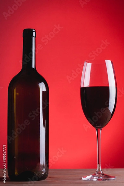 Fototapeta bottle of wine and glass with red wine, on red background, copy space