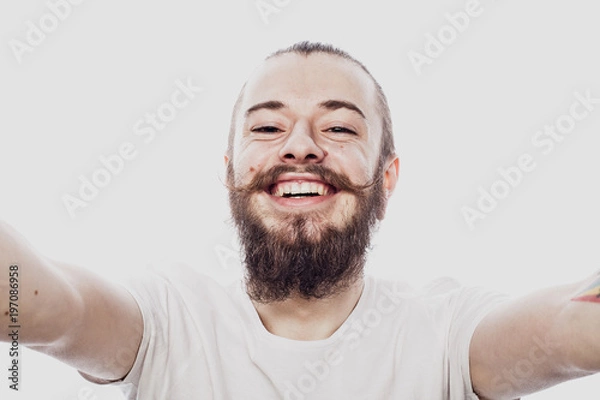 Obraz Close up portrait of a cheerful bearded man taking selfie over white background