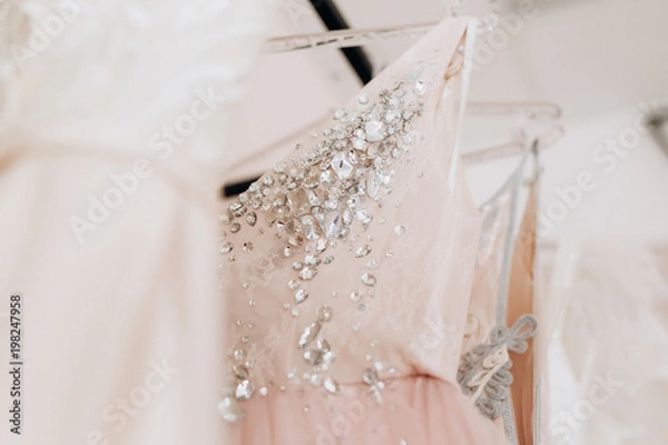 Fototapeta close-up embroidered with stones and sequins top pink wedding dress which hangs on a hanger among other dresses