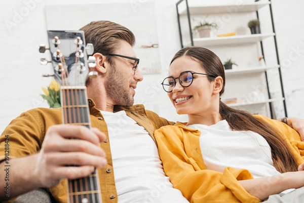 Fototapeta couple with guitar sitting on couch at home