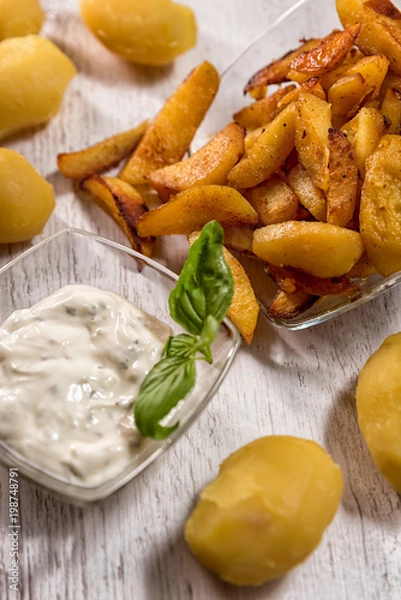 Fototapeta Roasted potatoes with herb sauce in glass dish placed on wooden table traditional European food