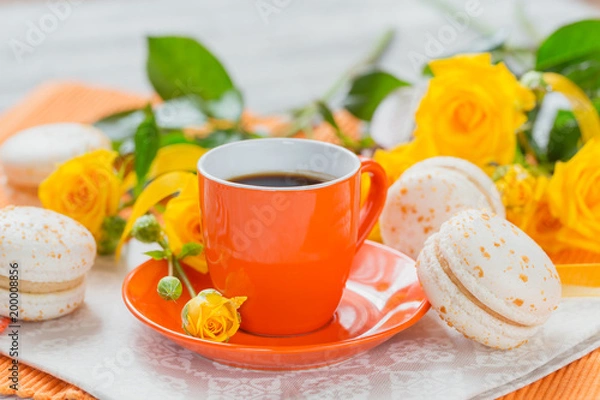 Fototapeta Orange cup of black coffee, yellow roses flowers and sweet pastel french macaroons