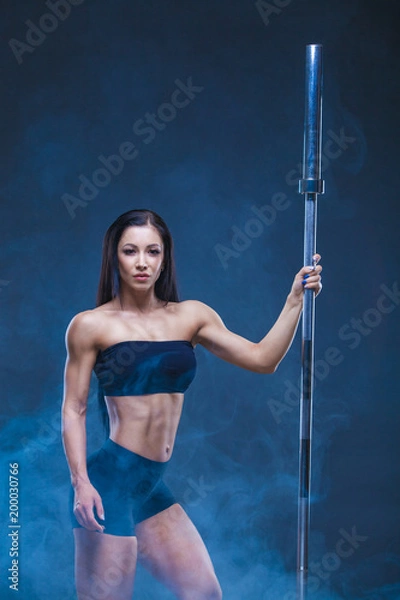 Fototapeta Brutal athletic sexy woman holds a barbell. The concept of exercise sports, advertising a gym.Isolated on a black background. Around the shrouds the model smoke.