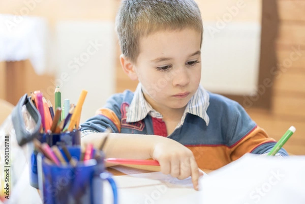 Fototapeta Candid portrait of a boy doing his homework and studying at home