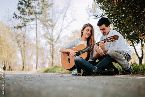 Obraz Guy teaching girl how to play guitar at the park.